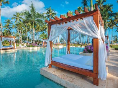 Luxuriöse Poolanlage mit Himmelbett, umgeben von Palmen und blauem Himmel.