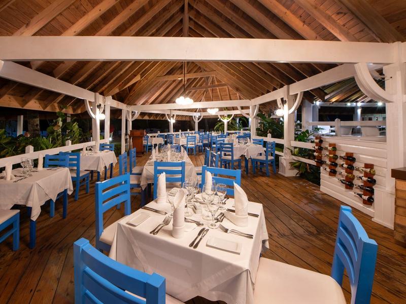 Elegantes Restaurant mit blauen Stühlen, weißen gedeckten Tischen, Holzboden und offenem Holzdach.