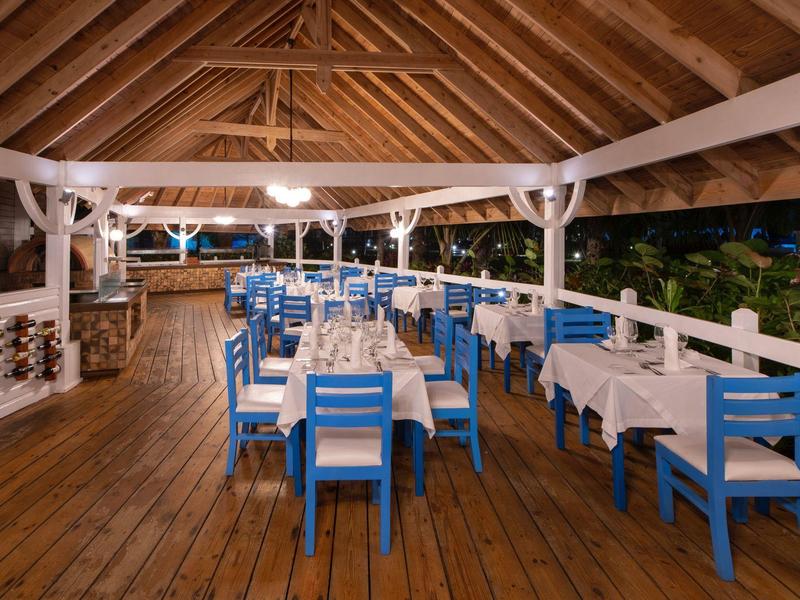 Offenes Restaurant mit Holzdecke, blauen Stühlen und weißen Tischen auf Holzfußboden bei Nacht.
