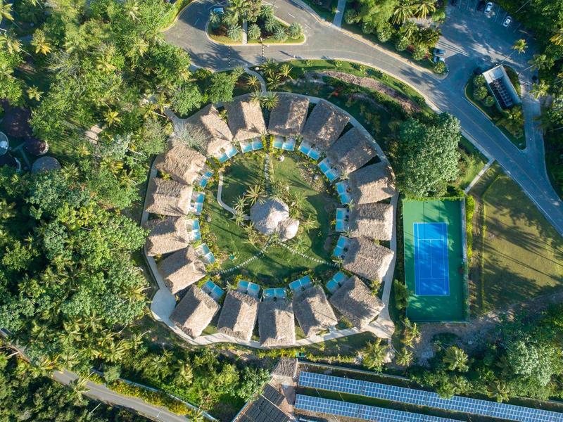Luftaufnahme eines runden Resorts mit Pool, umgeben von dichtem Grün und Straßen.