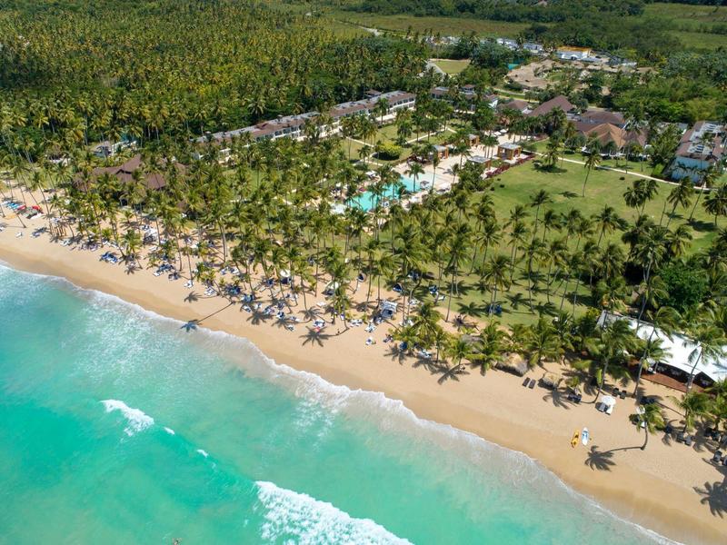 Langer Sandstrand mit türkisfarbenem Meer und dichtem Palmenwald entlang einer Hotelanlage.