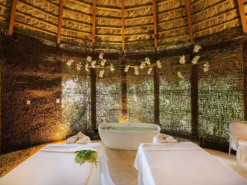 Gemütlicher Spa-Raum mit Holzdach, zwei Massageliegen, Wanne und natürlicher Dekoration.