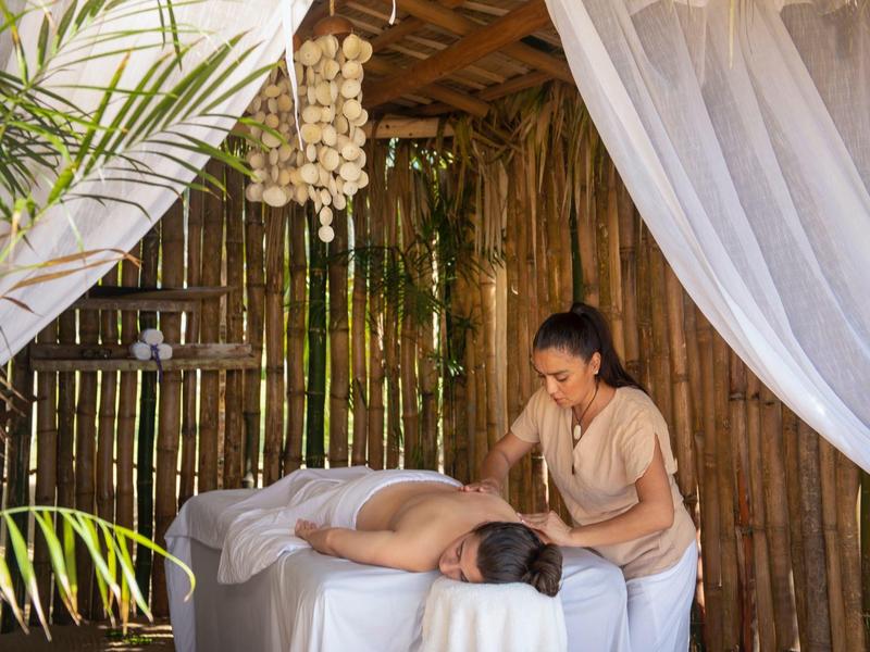 Frau erhält Massage in hellem Raum mit Bambuswänden und weißem Moskitonetz.