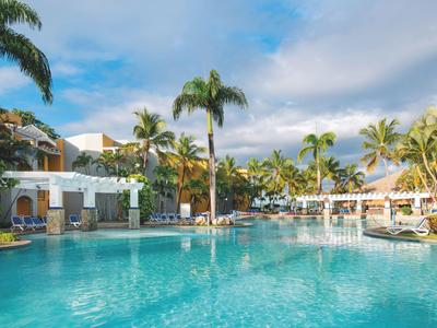 Großer Hotelpool mit Palmen und Liegestühlen unter blauem Himmel.