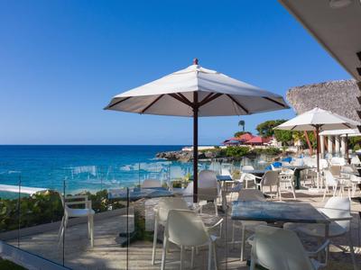 Terrasse eines Hotels mit Tischen, Stühlen und weißen Sonnenschirmen mit Meerblick.