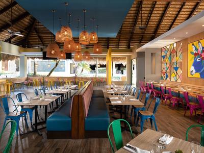 Modernes Restaurant mit bunten Stühlen, Holzboden und großen Kunstwerken an der Wand.