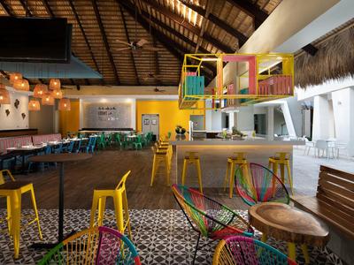 Bunte Sitzgelegenheiten und Barbereich in einem offenen, tropisch gestalteten Innenraum eines Hotels.