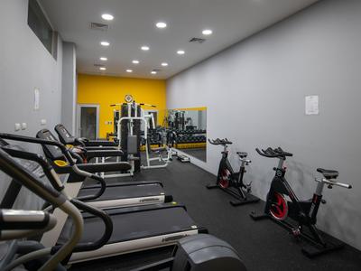 Moderner Fitnessraum mit Laufbändern, Fahrrädern und Kraftgeräten in neutralem Raum.