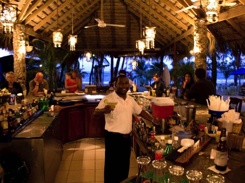 Gemütliche Bar mit Strohdach, Holzinterieur und warmem Licht, Personal dient Getränke.