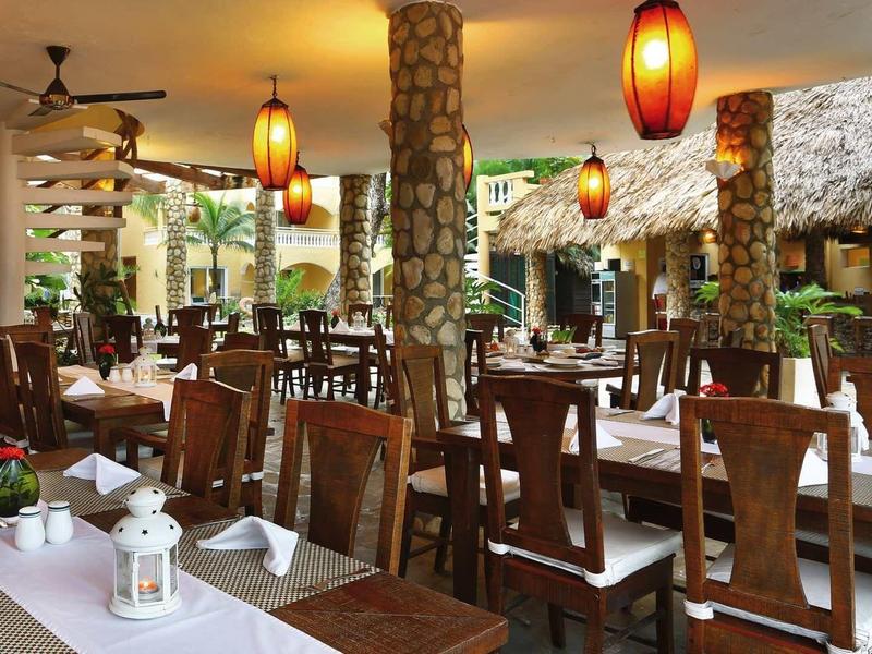 Offenes Restaurant mit Holzmöbeln, Steinsäulen, warmen Lampen und tropischer Atmosphäre.