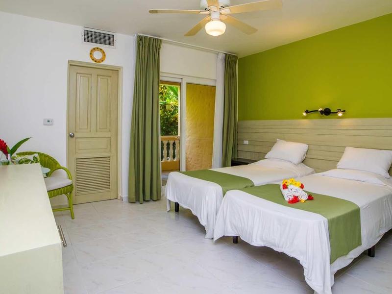 Modern eingerichtetes Hotelzimmer mit zwei Einzelbetten, grün-weißer Wandfarbe und Ventilator an der Decke.