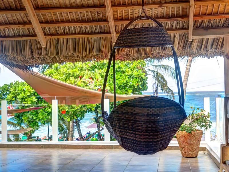 Hängesessel aus Rattan, Palmdach, Terrasse mit Meerblick, Pflanze im Topf, Sonnensegel.