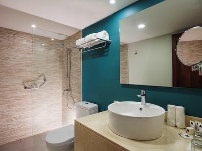 Moderner Badbereich mit hellen Fliesen, weißer Waschschale, großem Spiegel und Duschabtrennung.