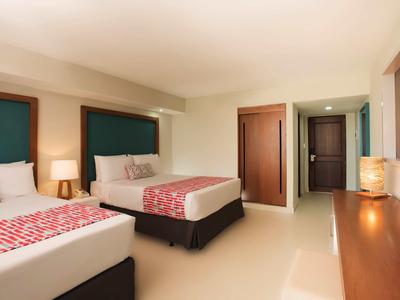 Modernes Hotelzimmer mit zwei Betten, Holzkommode, warmem Licht und schlichten Möbeln.