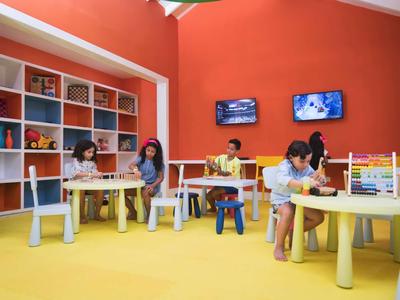 Kinder sitzen an runden Tischen in einem bunten Raum mit orangen Wänden und gelbem Boden.