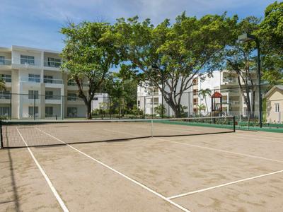 Een tennisbaan buiten omringd door bomen met meerlaagse gebouwen op de achtergrond.