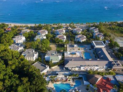 Küstenresort mit mehreren Gebäuden, Poolanlagen, viel Grün und Blick auf das blaue Meer.