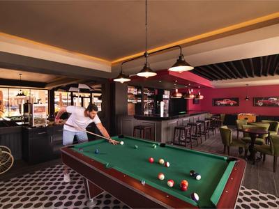 Innenraum einer Bar mit Billardtisch, Sitzgelegenheiten und zwei Personen beim Billardspielen.