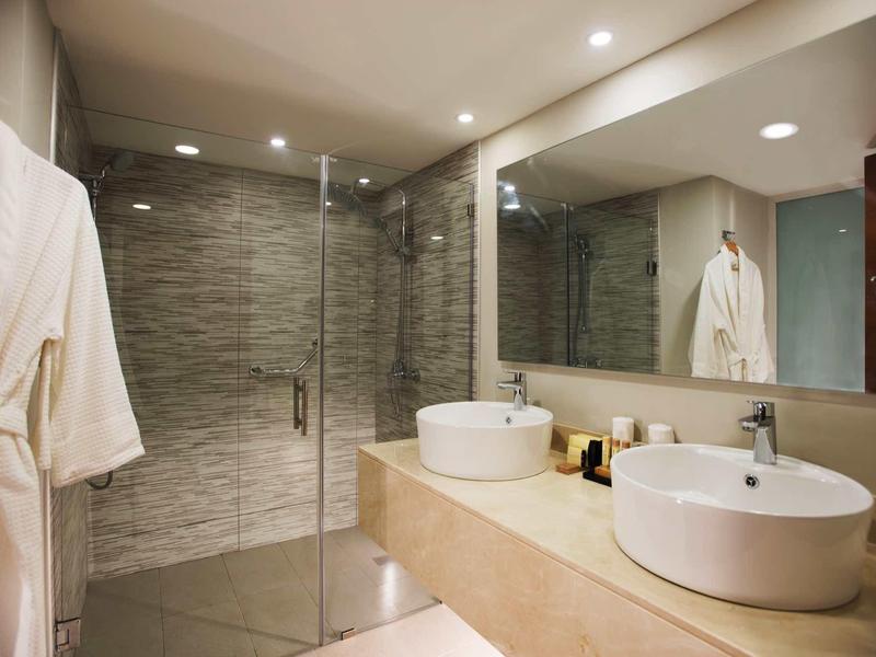 Modernes Badezimmer mit Doppelwaschbecken, großer Spiegel, Duschkabine und beigem Design.