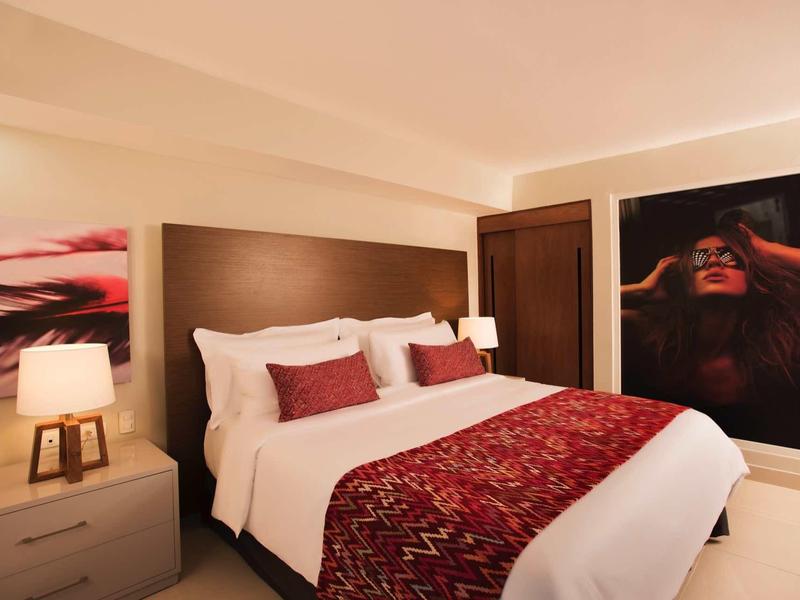 Schlafzimmer mit großem Bett, weißen Bettlaken, rotem Überwurf und zwei modernen Nachttischlampen.