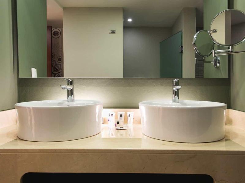 Moderne Badezimmer mit Doppelwaschbecken, großem Spiegel und grünen Wänden, weiße Handtücher hängen.