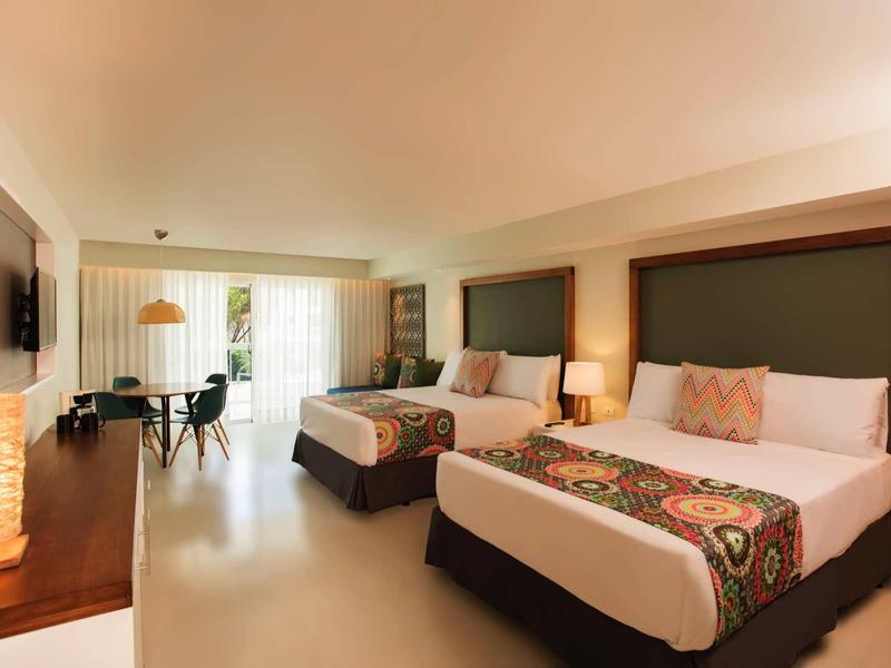 Modernes Hotelzimmer mit zwei Doppelbetten, hellem Fußboden und großem Fenster mit Blick ins Grüne.