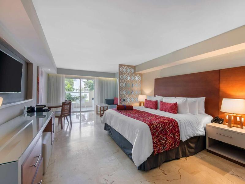 Modern eingerichtetes Hotelzimmer mit großem Bett, Schreibtisch, Fernseher und Balkon mit Meerblick.