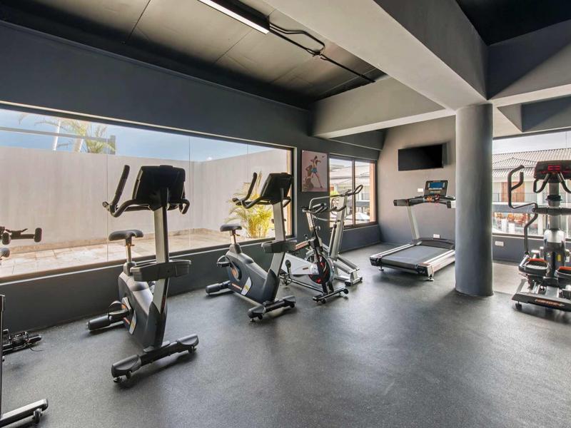 Moderner Fitnessraum mit mehreren Trainingsgeräten und großen Fenstern für Tageslicht.