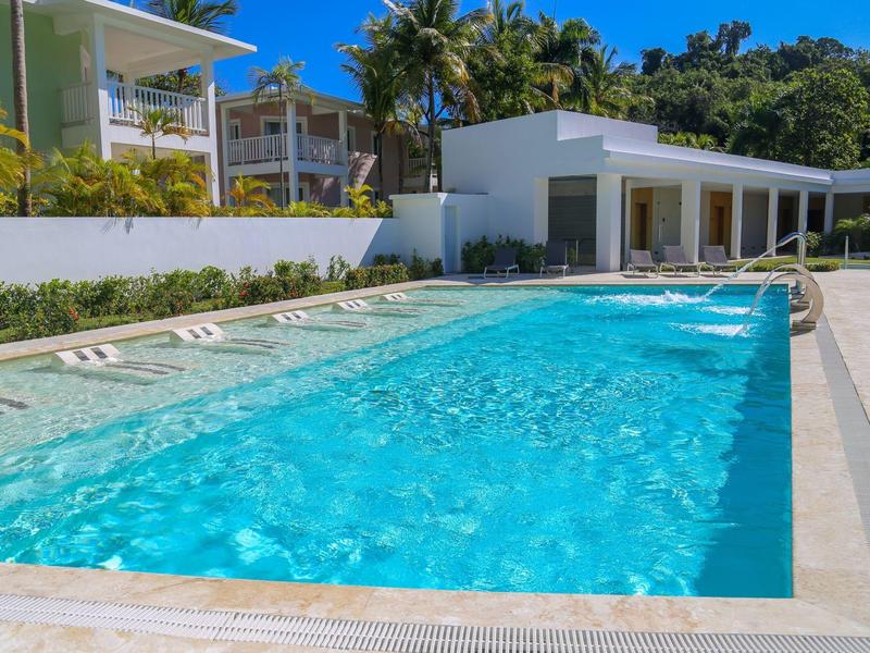 Moderner Außenpool mit klar blauem Wasser, umgeben von Liegestühlen und weißen Gebäuden.