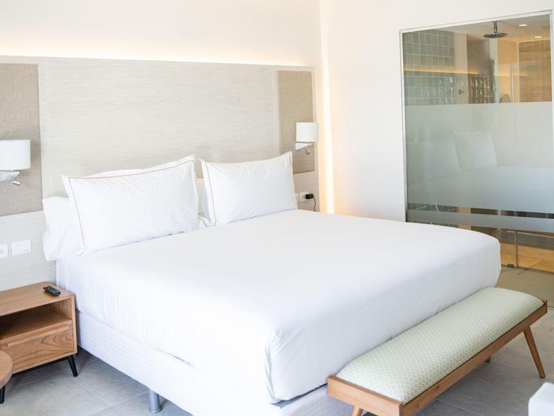 Helles, modernes Schlafzimmer mit großem weißen Bett, Holznachttisch und Sitzbank am Fußende.