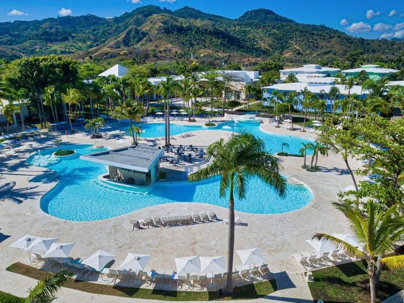 Großer Hotelpool mit Liegestühlen und Bergen im Hintergrund an einem sonnigen Tag.