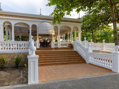 Elegant white building with wide staircase and columns, surrounded by green trees.