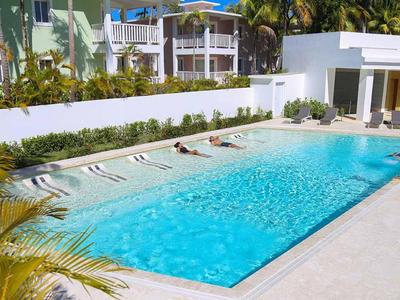 Moderner Außenpool mit Liegestühlen und Sonnenschirmen in einem Hotelgarten.