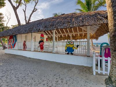 Strandhütte mit Strohdach und bunten Figuren am Sandstrand unter blauen Himmel.