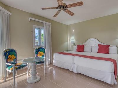 Helles Schlafzimmer mit großem Bett, weißen Möbeln, zwei bunten Stühlen und Deckenventilator.