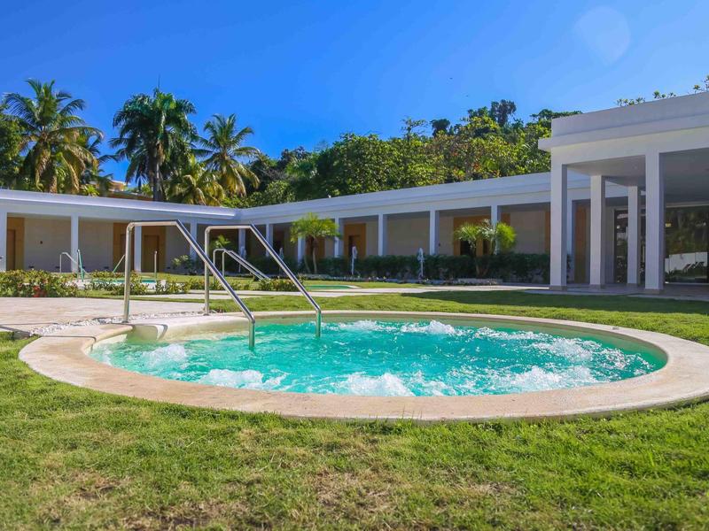 Runder Whirlpool mit sprudelndem Wasser vor modernem Gebäude und Palmen im Hintergrund.