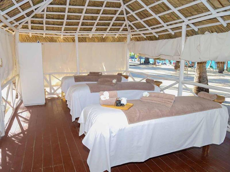 Offener Massagebereich mit mehreren Massageliegen unter einem Dach mit Blick auf das Wasser.