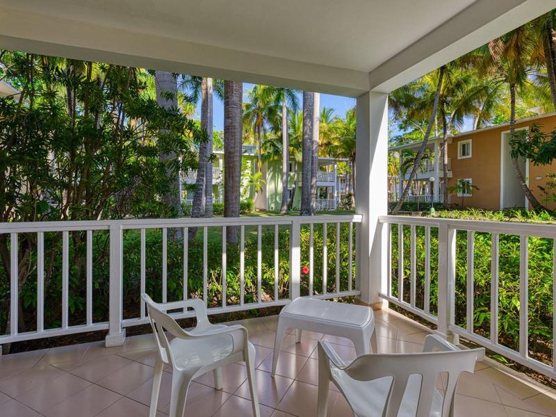 Überdachter Balkon mit weißen Stühlen und Tisch, umgeben von tropischer Vegetation.