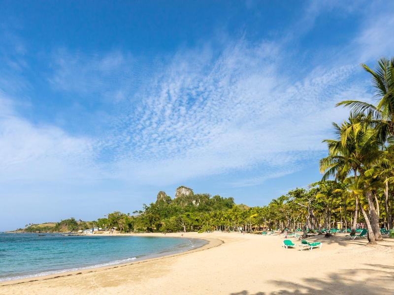 Strand mit hellem Sand, blauen Meer, Palmen und blauem Himmel mit Wolken.