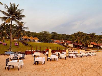 Strandrestaurant mit weißen Tischtüchern, Palmen und Hütten im Hintergrund bei Sonnenuntergang.
