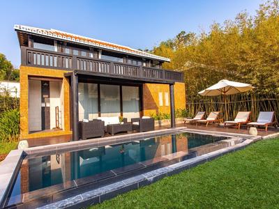 Moderne Holzvilla mit großem Pool, grüner Wiese, Liegestühlen und Sonnenschirm bei Sonnenuntergang.