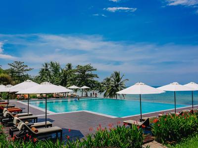 Moderner Pool mit Liegestühlen und weißen Sonnenschirmen vor blauem Himmel und Meerblick