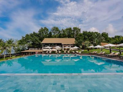 Großer Pool vor einem Hotel mit Liegestühlen und Sonnenschirmen unter blauem Himmel