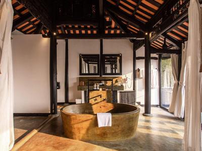 Rustikale Badewanne aus Kupfer in einem offenen Raum mit Holzbalken und weißen Vorhängen.