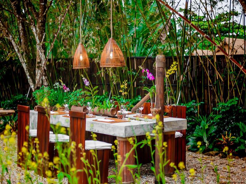Rustikaler Gartentisch aus Holz mit Steckdosen, umgeben von grünen Pflanzen und hängenden Lampen.