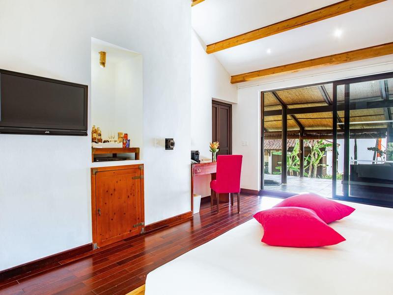 Modernes Schlafzimmer mit Holzboden, weißer Wand, rotem Stuhl und Zugang zu Terrasse durch Glasschiebetüren.