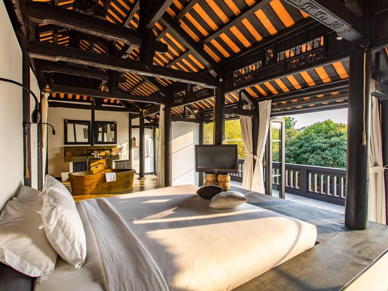 Geräumiges Schlafzimmer mit Holzbalken, großem Bett, TV und Balkon mit Naturblick.