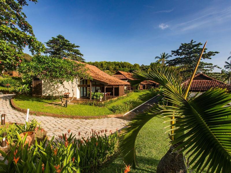 Haus mit rotem Dach und Steinmauern, umgeben von Grün, Blumen und einem gepflasterten Weg.