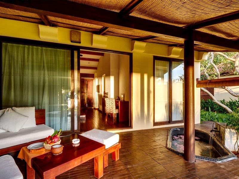 Gemütliche Terrasse mit Holzsäulen, Sofa, Tisch und offenen Türen zu einem hellen Innenraum.