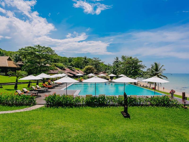 Großer Infinity-Pool mit Liegestühlen und Sonnenschirmen, umgeben von grünem Rasen und Meerblick.